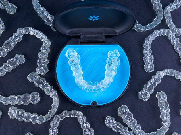 Bird’s eye view of several Invisalign trays surrounding carrying case with black background