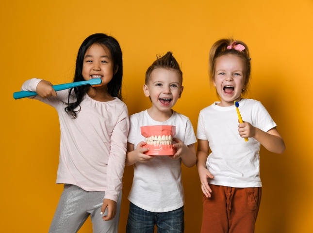 Two kids holding giant toothbrushes with a third kid holding a model of teeth
