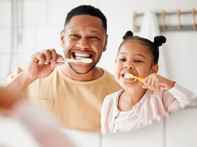 A girl and her father brushing their teeth 