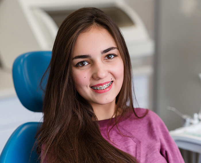 Teenage girl with traditional braces smiling in dental chair