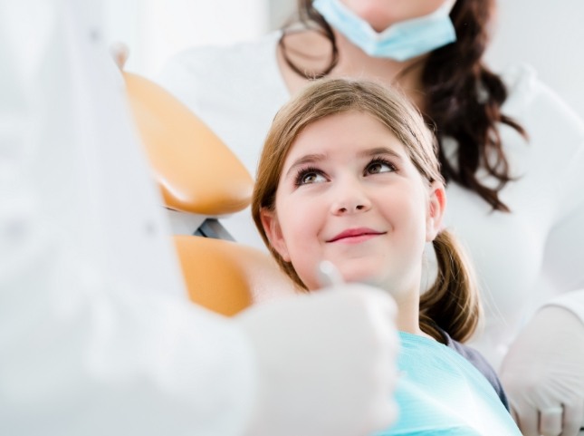 Young girl in dental chair smiling at her dentist