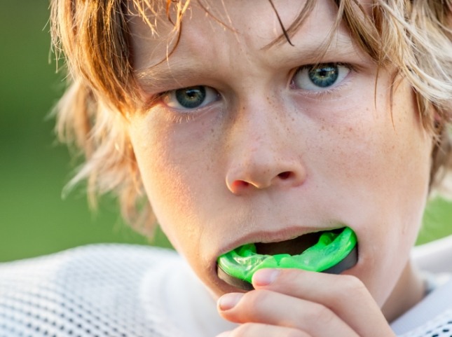 Boy placing a green athletic mouthguard over his teeth