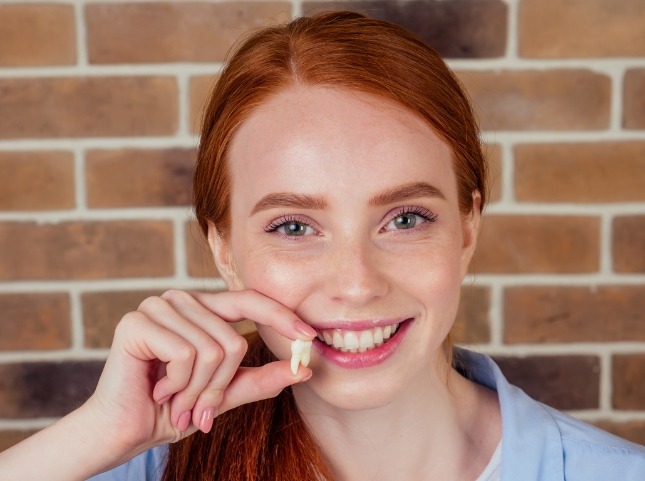 Smiling young woman holding an extracted tooth