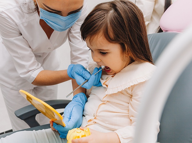 Dentist showing little girl her teeth with handheld mirror