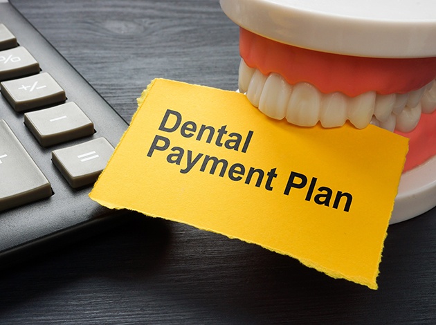 Artificial teeth biting a yellow paper that reads “Dental Payment Plan”