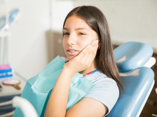 Teenage girl in dental chair holding her cheek in pain