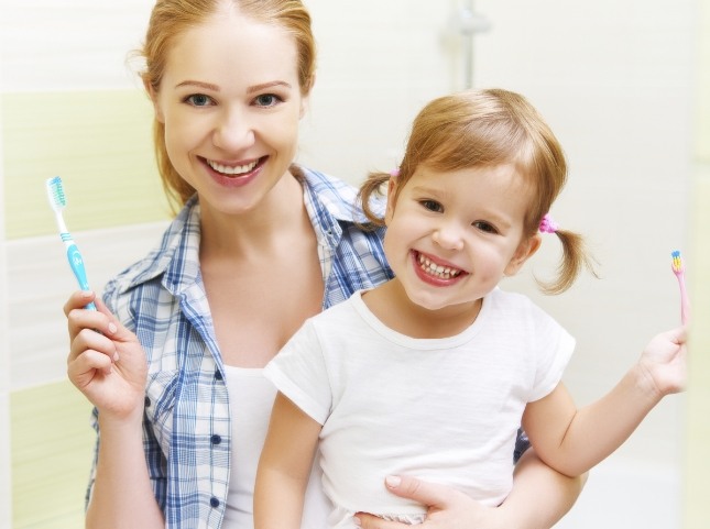 Smiling mother and daughter holding toothbrushes