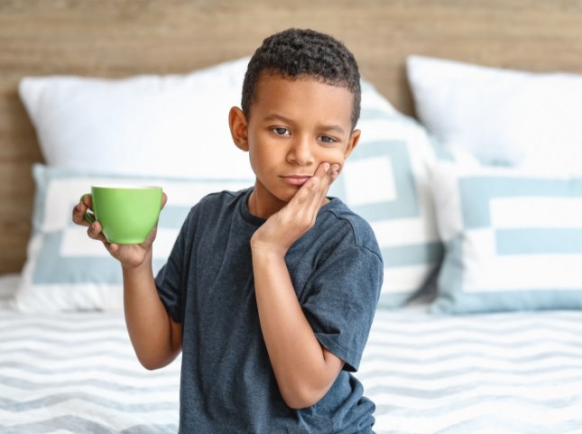Young boy with a green coffee mug holding his cheek in pain