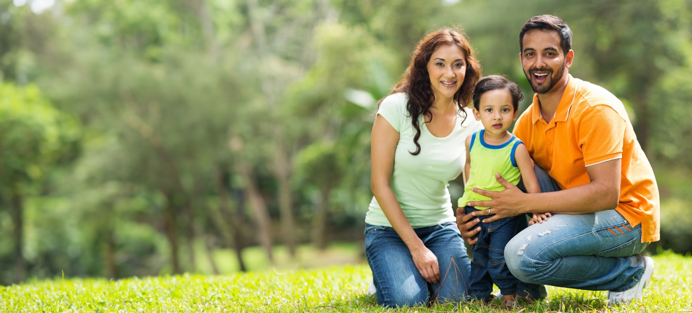 Man and woman smiling outdoors with their young son