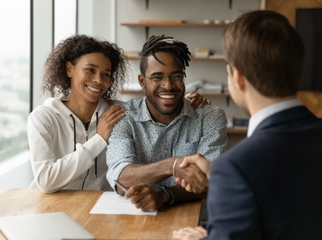 Smiling man shaking hands with person sitting across desk