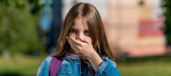 Young girl in denim jacket covering her mouth