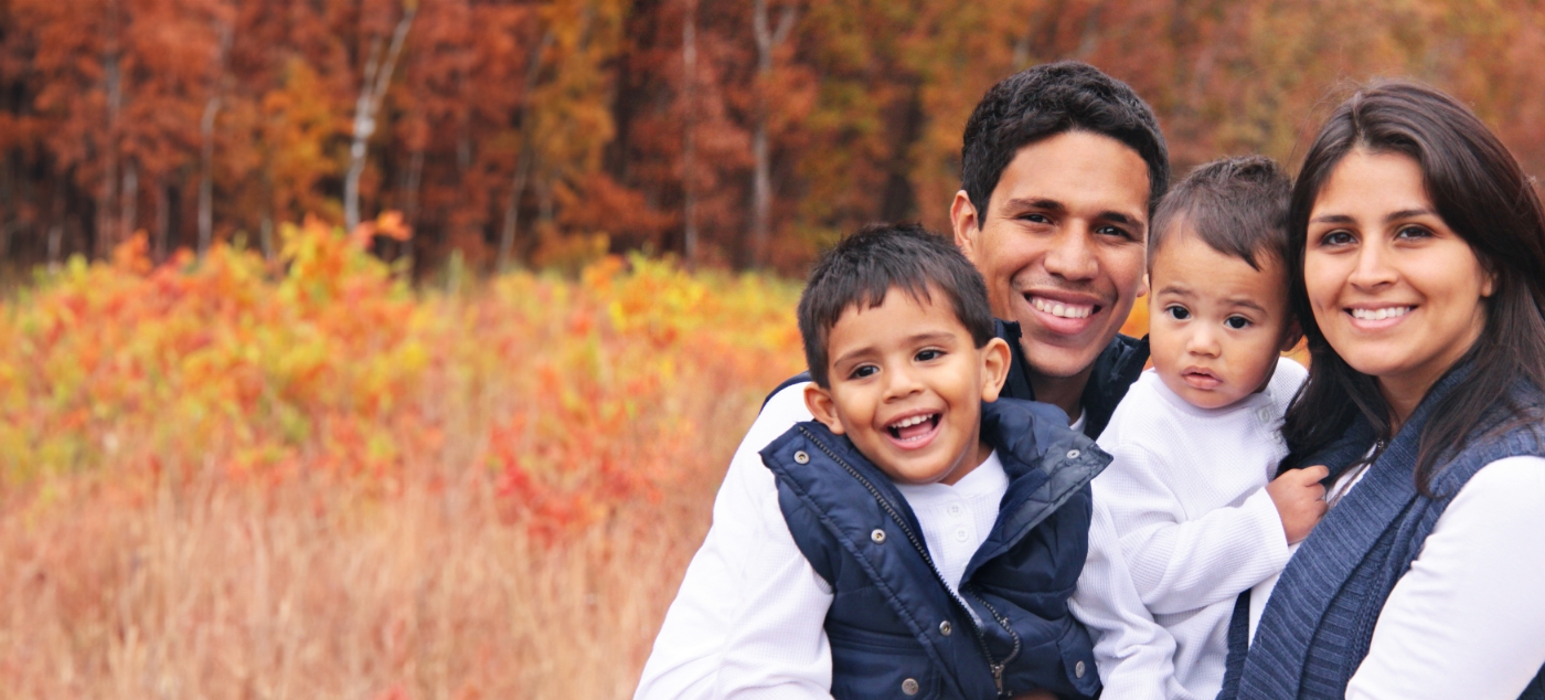 Family of four smiling outdoors with autumn trees in background