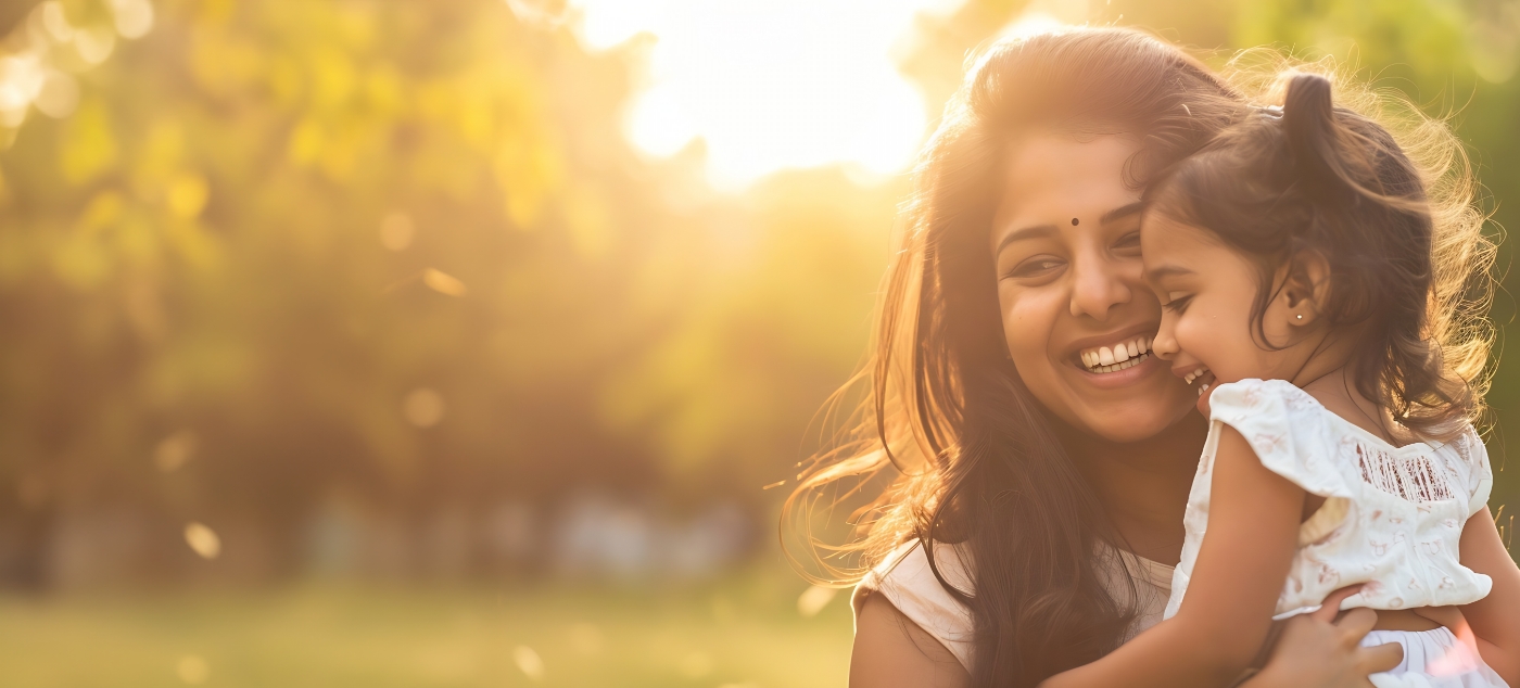 Smiling woman holding her daughter outdoors on sunny day