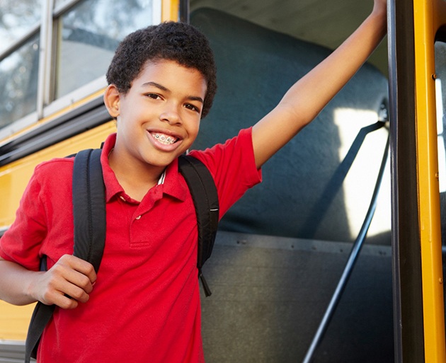a boy with braces leaning up against a school bus