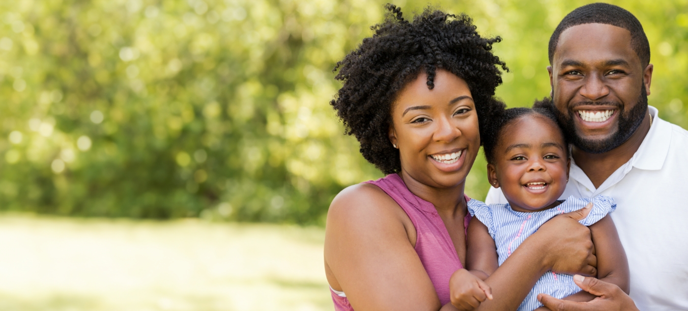 Smiling man and woman holding their baby outdoors