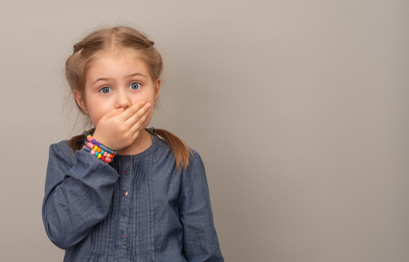 A little girl covering her mouth over a gray background
